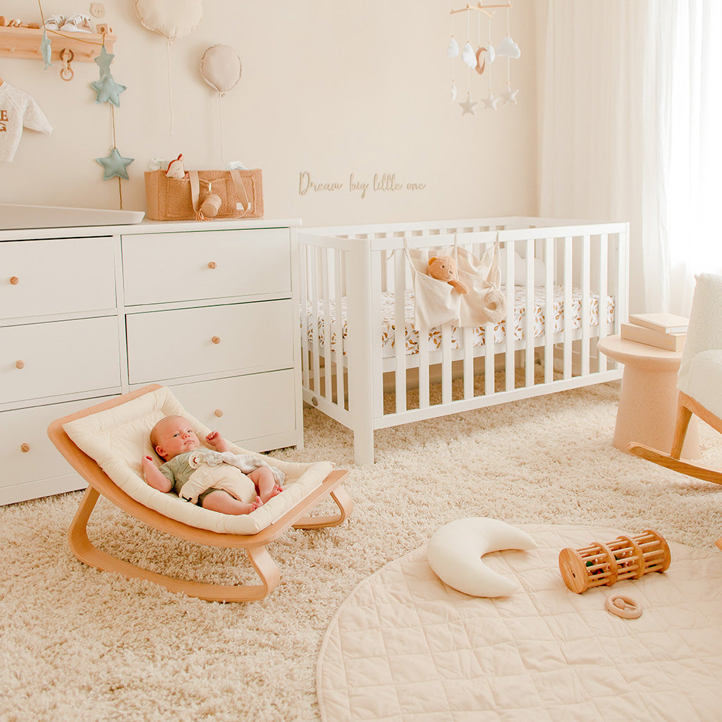 Nursery room with a baby in a wooden floor chair, surrounded by toys, furniture and organic play mat.