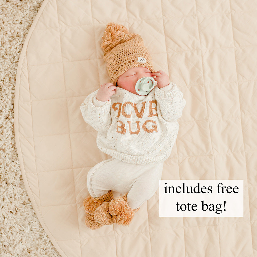 Newborn baby in a cute outfit with a pacifier, lying on a cotton organic play mat.